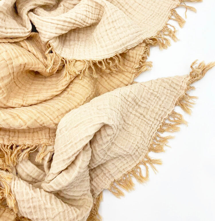 a close up of the mustard throw bed and couch blanket made with 100% light cotton, with tassels