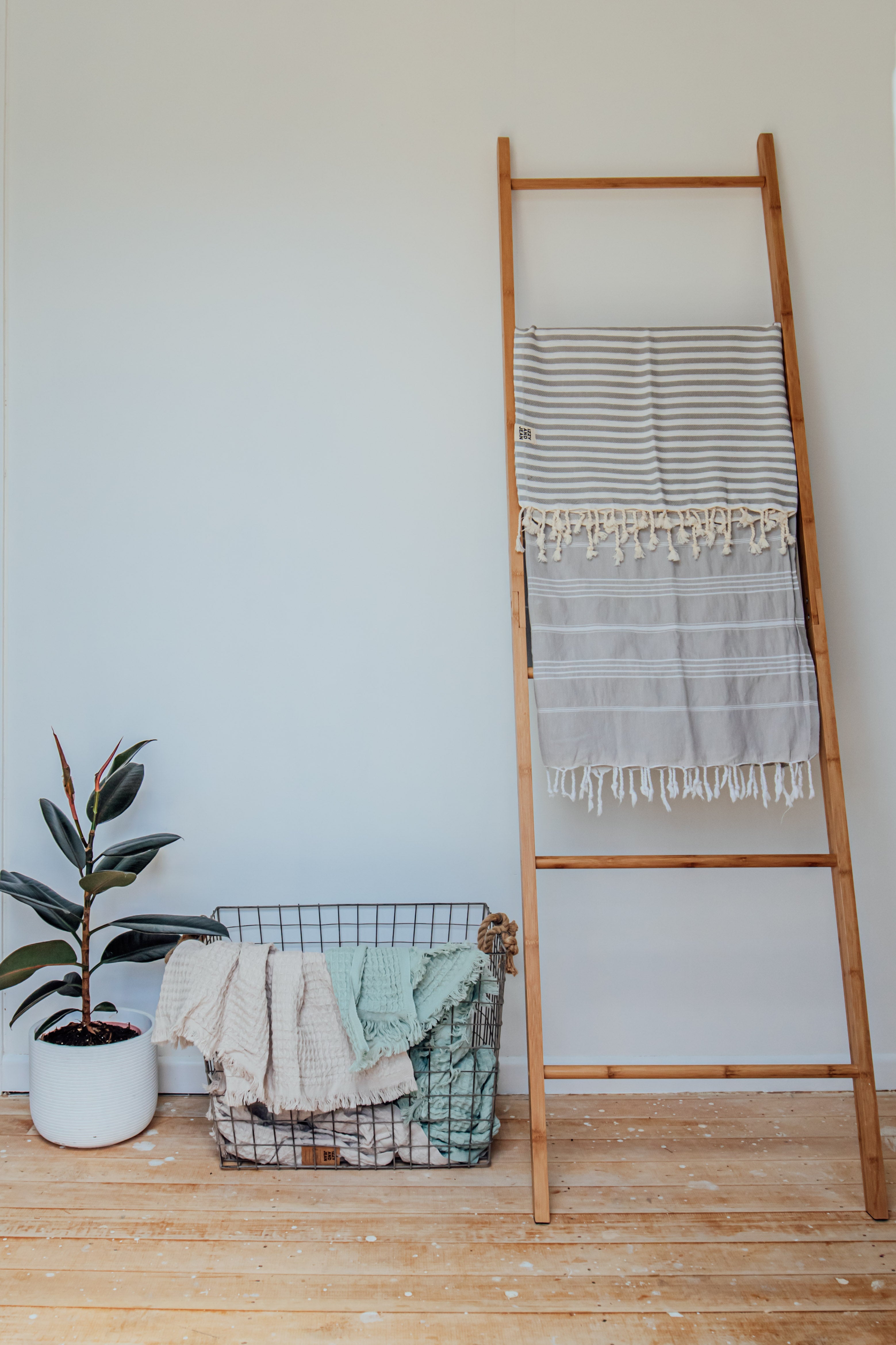 A pale grey Turkish towel with white stripes and tassels on the bottom edge folder over a rung on a wooden ladder